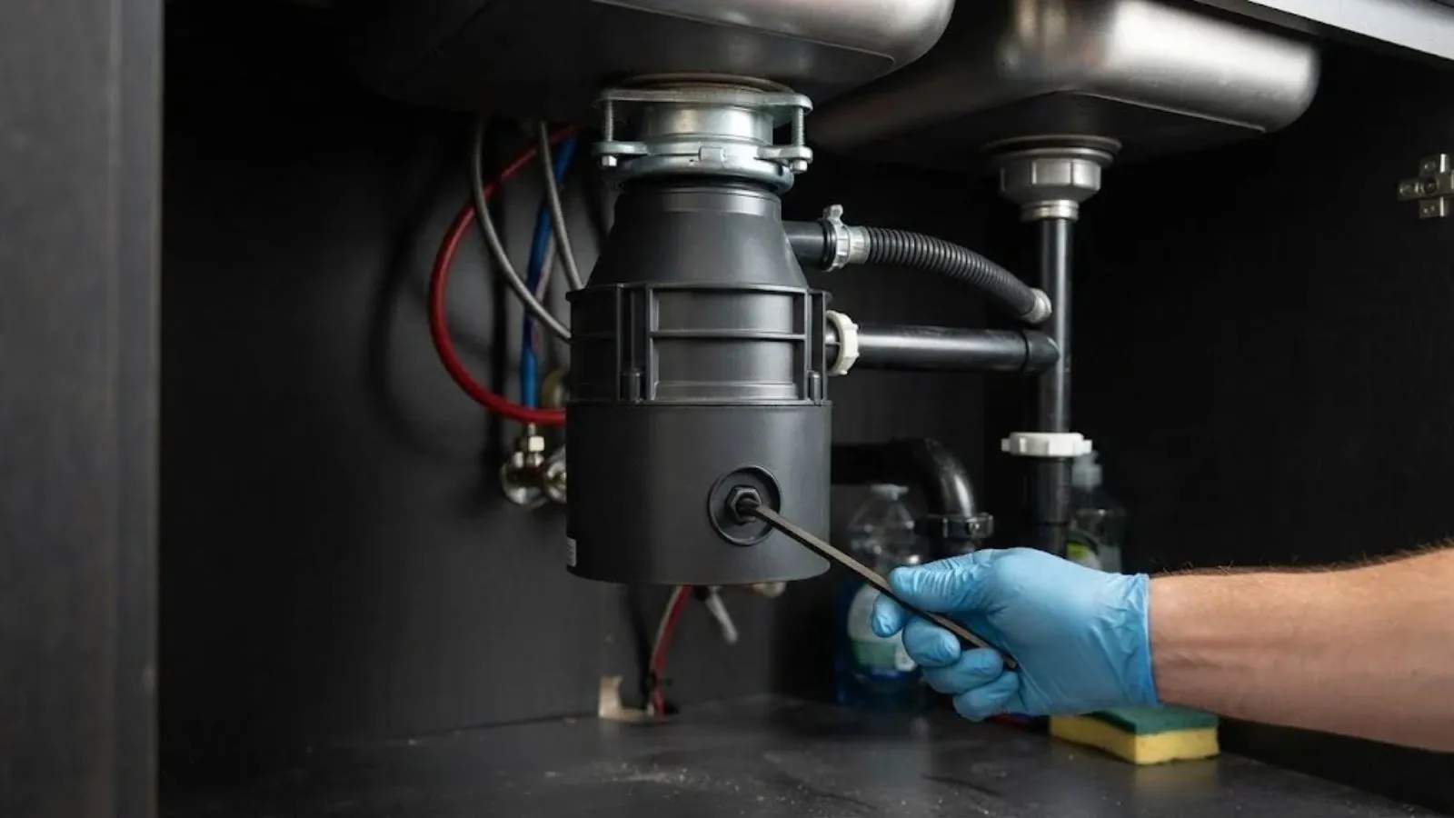 Hand using a hex key on a garbage disposal under a kitchen sink