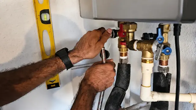 Hands checking valves and fittings under a wall-mounted tankless water heater with a level